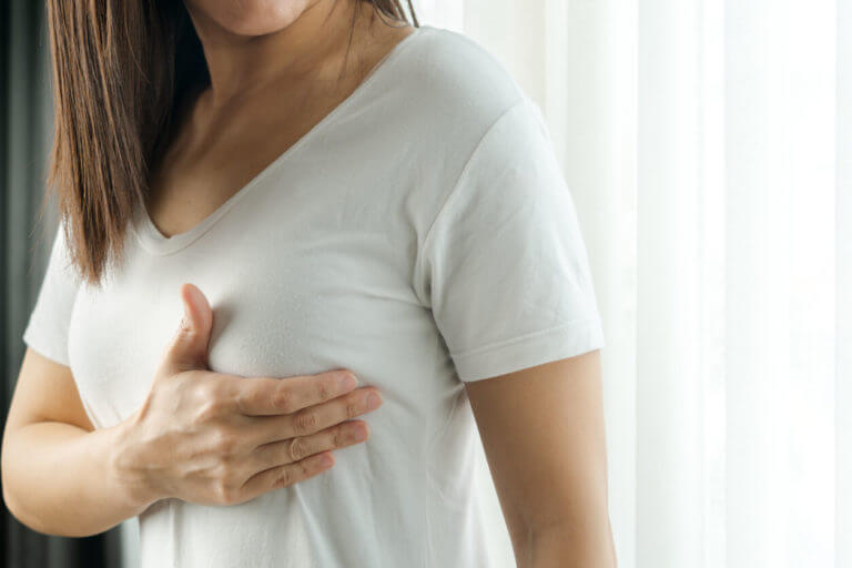 A woman is examining her breasts for lumps as a way to check for signs of breast cancer.