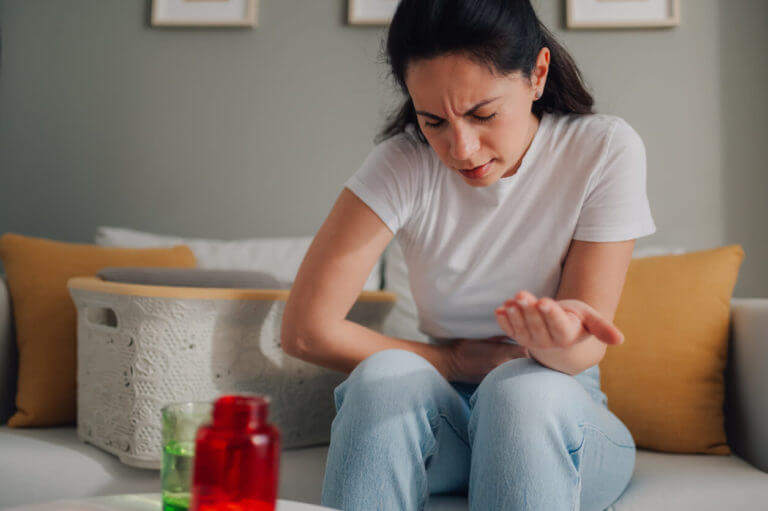 A woman feeling abdominal pain while sitting on sofa at home due to endometriosis.