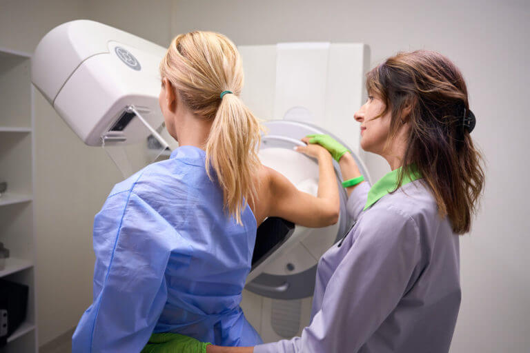 Radiographer preparing female client for digital breast tomosynthesis type of mammograms.